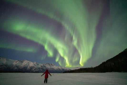 peron standing under aurora with mountains in the background in Alaska